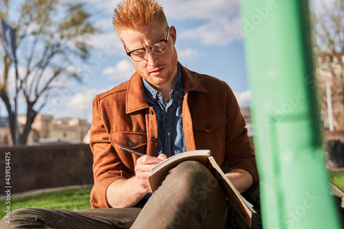 Man wearing glasses writing into notebook while spending time at the nature