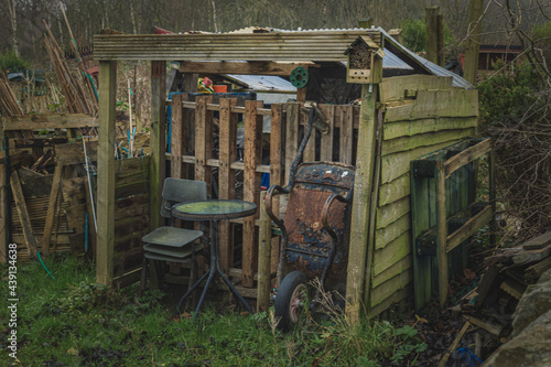 Fototapeta A makeshift gritty old garden shed with a rusty tired wheelbarrow propped up aga