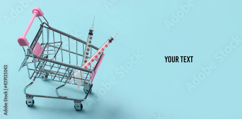 Syringes in a supermarket trolley on a blue background. Copy space