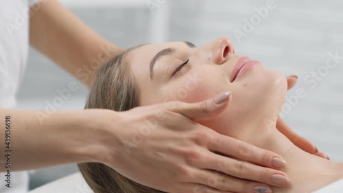 Side view portrait of young smiling beautiful woman lying on procedure massage for face in professional beauty salon. Concept of process special procedure for improvements skin face and body. 