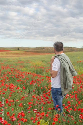 A man in a white t-shirt and jeans stands in a blooming poppy field and looks at the horizon. Summer countryside vacation theme.