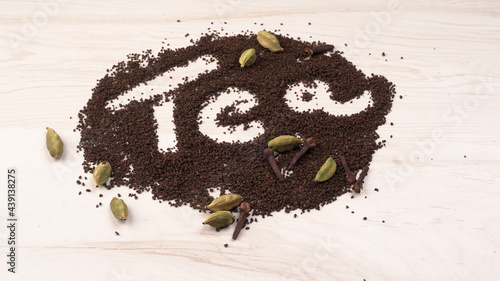 Black Tea Powder or dry dust tea powder, chai patti isolated in wooden bowl with Cardamom, Clove and Ginger. photo