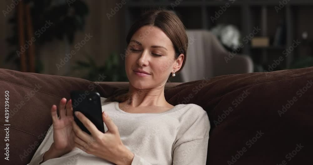 Young woman relax on couch with smartphone, spend free time at home looks at cell phone screen, typing message to friend in social network, shopping dating online services client, web surfing concept Young woman relax on couch with smartphone, spend free time at home looks at cell phone screen, typing message to friend in social network, shopping dating online services client, web surfing concept