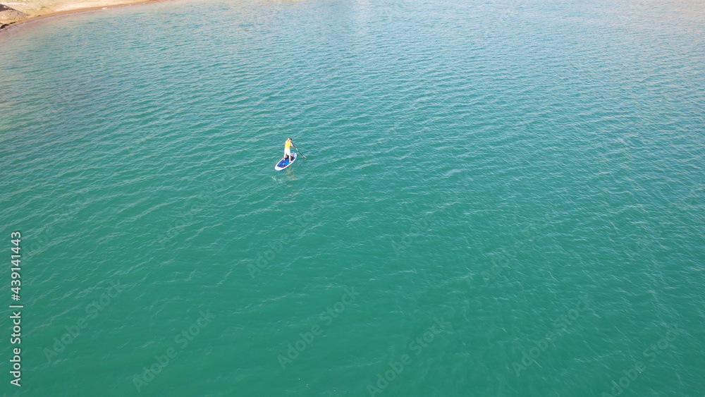 A group of people ride sup surfing in the lake. Aerial view from the drone of the green water and rocky beaches. Inflatable sapboard board. Trees and bushes grow on the bank of Kapchagai.