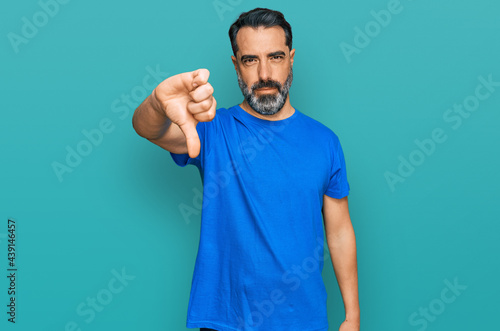 Middle aged man with beard wearing casual blue t shirt looking unhappy and angry showing rejection and negative with thumbs down gesture. bad expression.