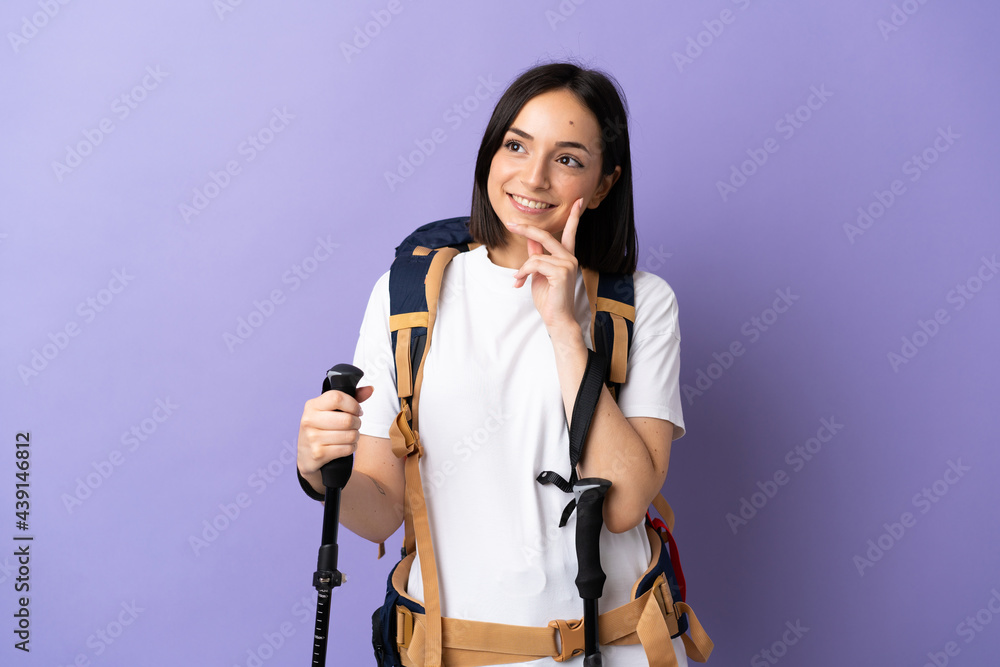 Young caucasian woman with backpack and trekking poles isolated on blue background thinking an idea while looking up