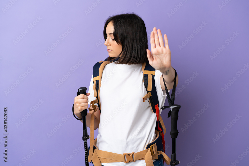Young caucasian woman with backpack and trekking poles isolated on blue background making stop gesture and disappointed Young caucasian woman with backpack and trekking poles isolated on blue background making stop gesture and disappointed