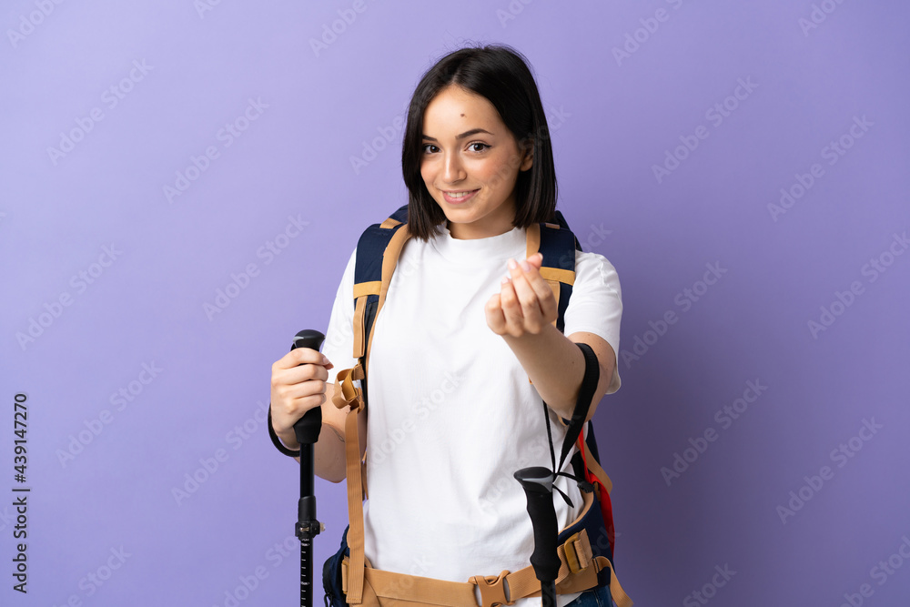 Young caucasian woman with backpack and trekking poles isolated on blue background making money gesture