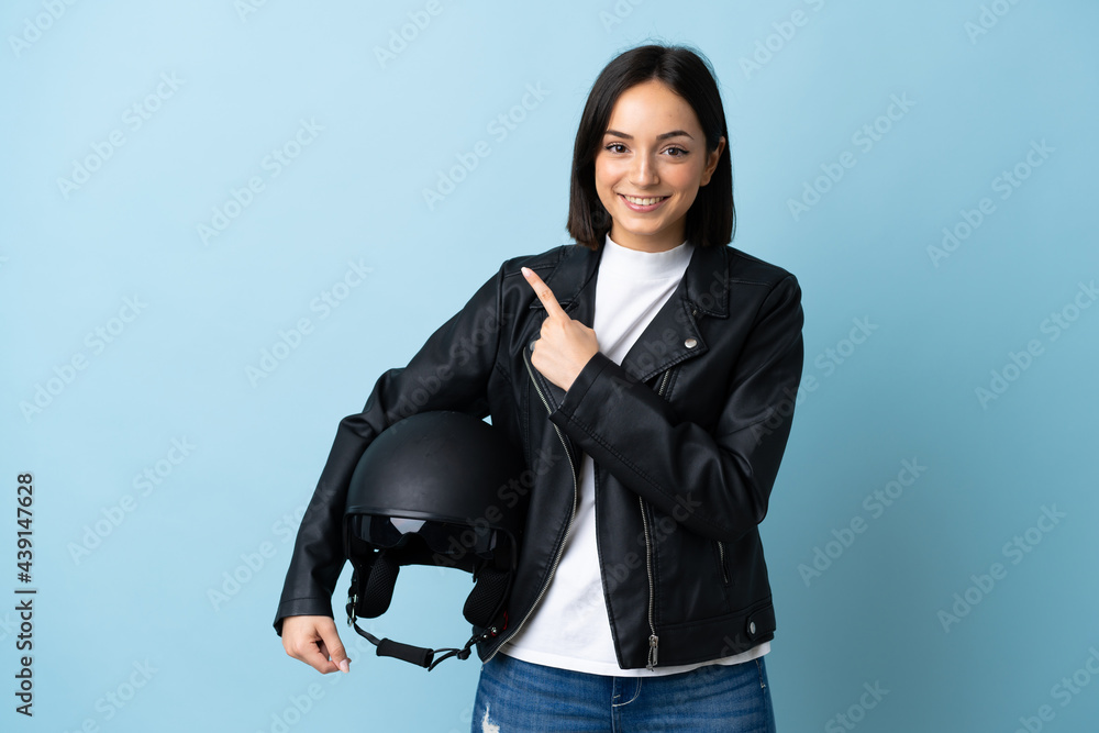 Woman holding a motorcycle helmet isolated on blue background pointing to the side to present a product Woman holding a motorcycle helmet isolated on blue background pointing to the side to present a product