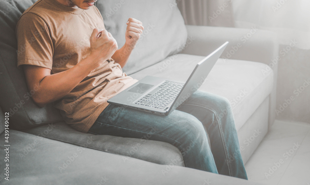 Naklejka premium happy man with laptop sitting on sofa.Man with his arms up for having had some achievement.