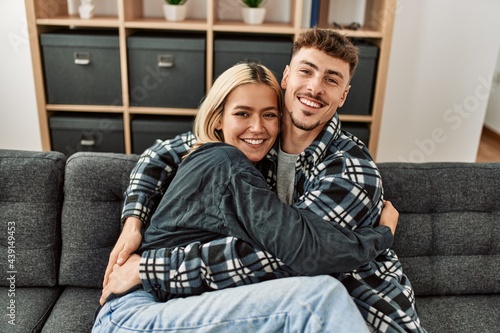 Young caucasian couple smiling happy and hugging sitting on the sofa at home.