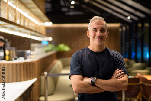 Portrait of man inside coffee shop at night smiling with arms crossed