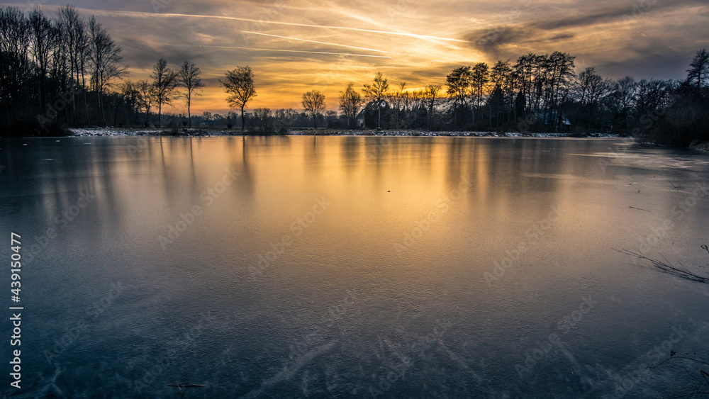 Dusk at winter evening on a frozen lake with silhouettes trees and reflection