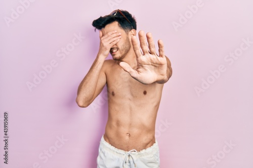 Young hispanic man wearing swimwear shirtless covering eyes with hands and doing stop gesture with sad and fear expression. embarrassed and negative concept. photo