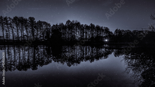 Small lake surrounded by trees reflecting the stars on the night sky