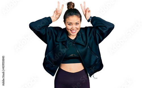 Young hispanic girl wearing sportswear posing funny and crazy with fingers on head as bunny ears, smiling cheerful © Krakenimages.com