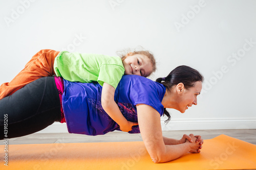 Active boy laying on his mother while she is standing in plank