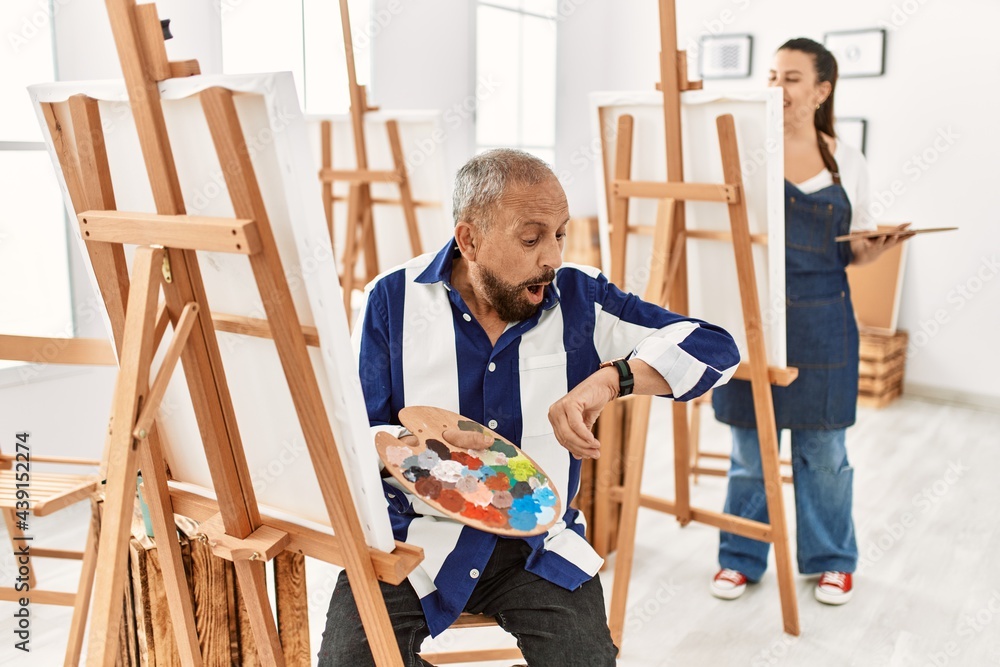 Senior artist man at art studio looking at the watch time worried, afraid of getting late