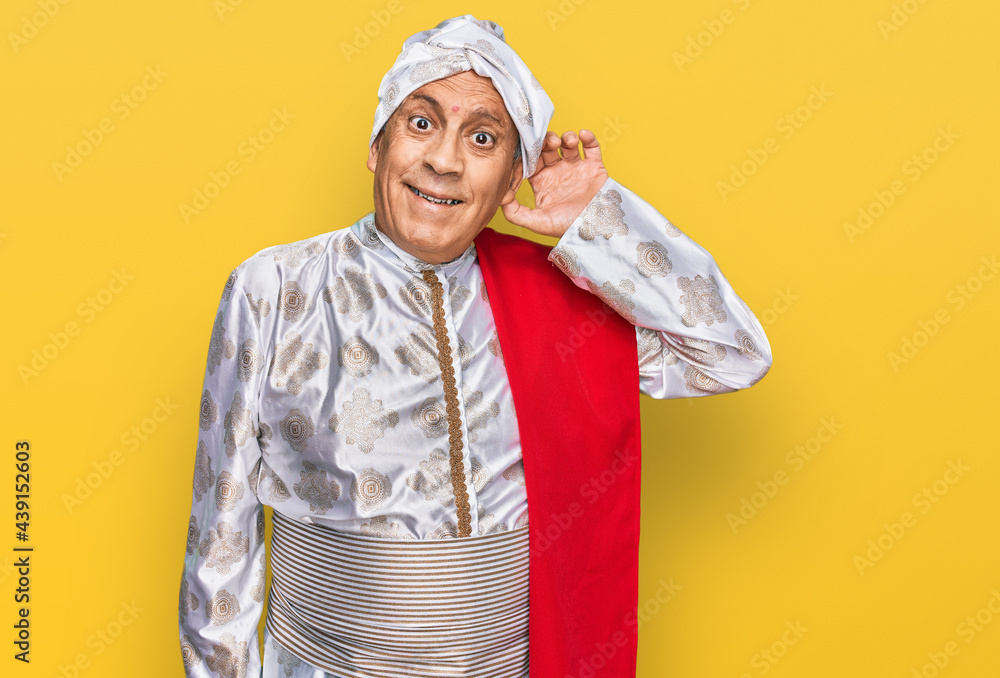 Senior hispanic man wearing tradition sherwani saree clothes smiling with hand over ear listening an hearing to rumor or gossip. deafness concept. Senior hispanic man wearing tradition sherwani saree clothes smiling with hand over ear listening an hearing to rumor or gossip. deafness concept.