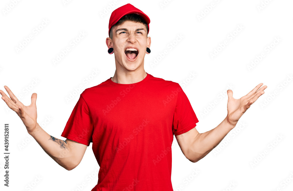 Young caucasian boy with ears dilation wearing delivery uniform and cap celebrating mad and crazy for success with arms raised and closed eyes screaming excited. winner concept Young caucasian boy with ears dilation wearing delivery uniform and cap celebrating mad and crazy for success with arms raised and closed eyes screaming excited. winner concept