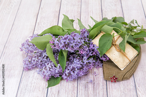 Victory Day. 9th May. A bouquet of lilacs, old photos and a soldier's cap / On the photo is a dummy of a soldier's cap