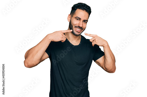 Hispanic man with beard wearing casual black t shirt smiling cheerful showing and pointing with fingers teeth and mouth. dental health concept. © Krakenimages.com