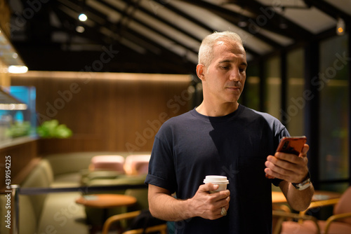 Portrait of man inside coffee shop at night using mobile phone