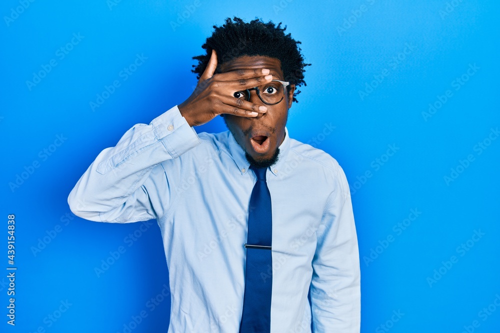 Young african american man wearing business clothes peeking in shock covering face and eyes with hand, looking through fingers afraid