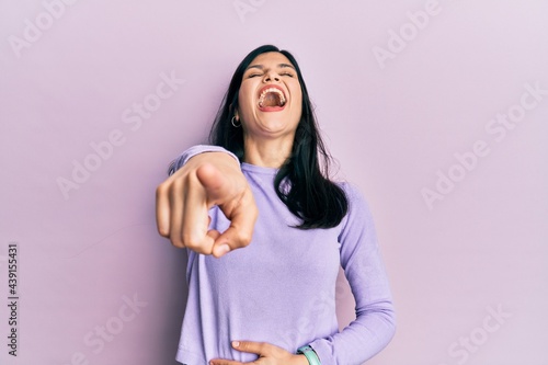 Young hispanic woman wearing casual clothes laughing at you, pointing finger to the camera with hand over body, shame expression