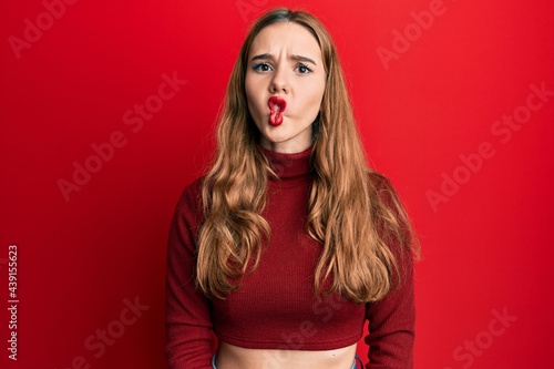 Young blonde woman wearing turtleneck sweater making fish face with lips, crazy and comical gesture. funny expression.