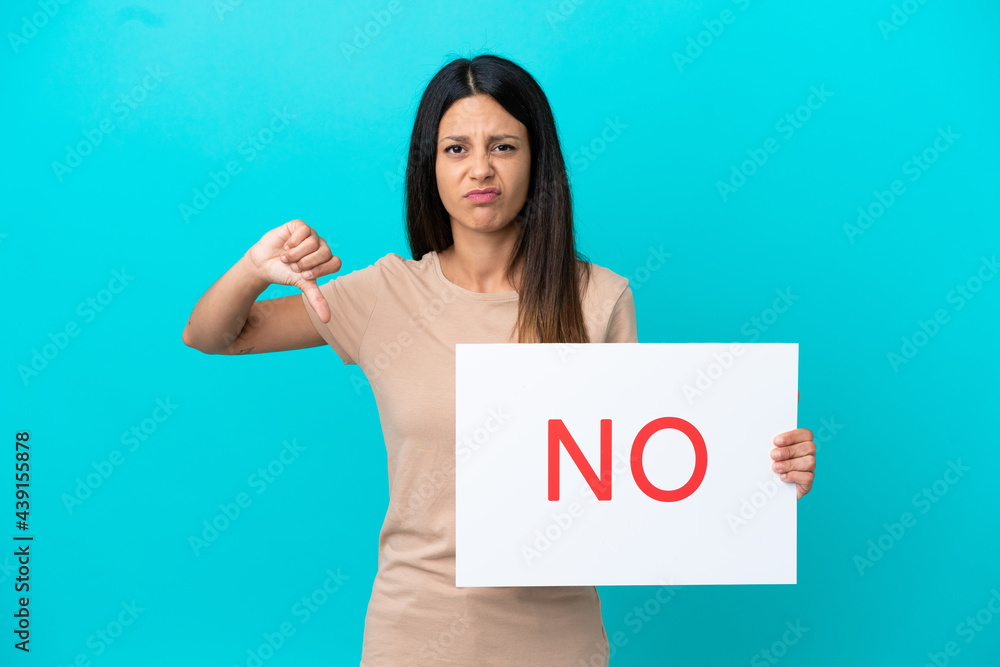 Young woman over isolated background holding a placard with text NO and doing bad signal Young woman over isolated background holding a placard with text NO and doing bad signal