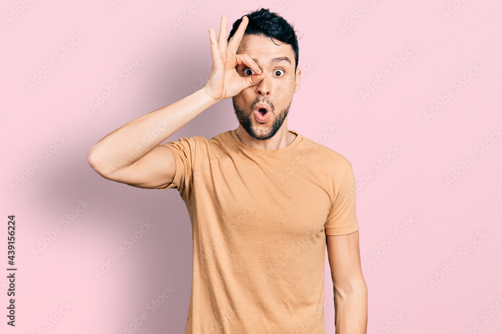 Hispanic man with beard wearing casual t shirt doing ok gesture shocked with surprised face, eye looking through fingers. unbelieving expression. Hispanic man with beard wearing casual t shirt doing ok gesture shocked with surprised face, eye looking through fingers. unbelieving expression.