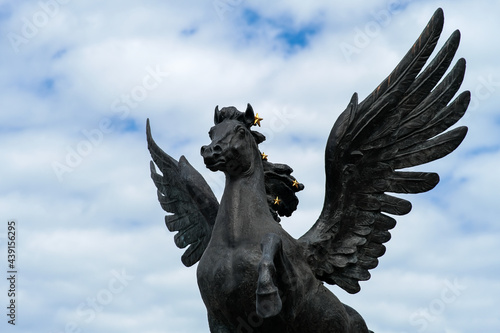 Bronze sculpture of a pegasus horse with wings. Blue sky background with clouds. Saint-Petersburg. Russia. June 2, 2021