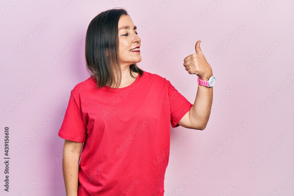 Middle age hispanic woman wearing casual clothes looking proud, smiling doing thumbs up gesture to the side Middle age hispanic woman wearing casual clothes looking proud, smiling doing thumbs up gesture to the side