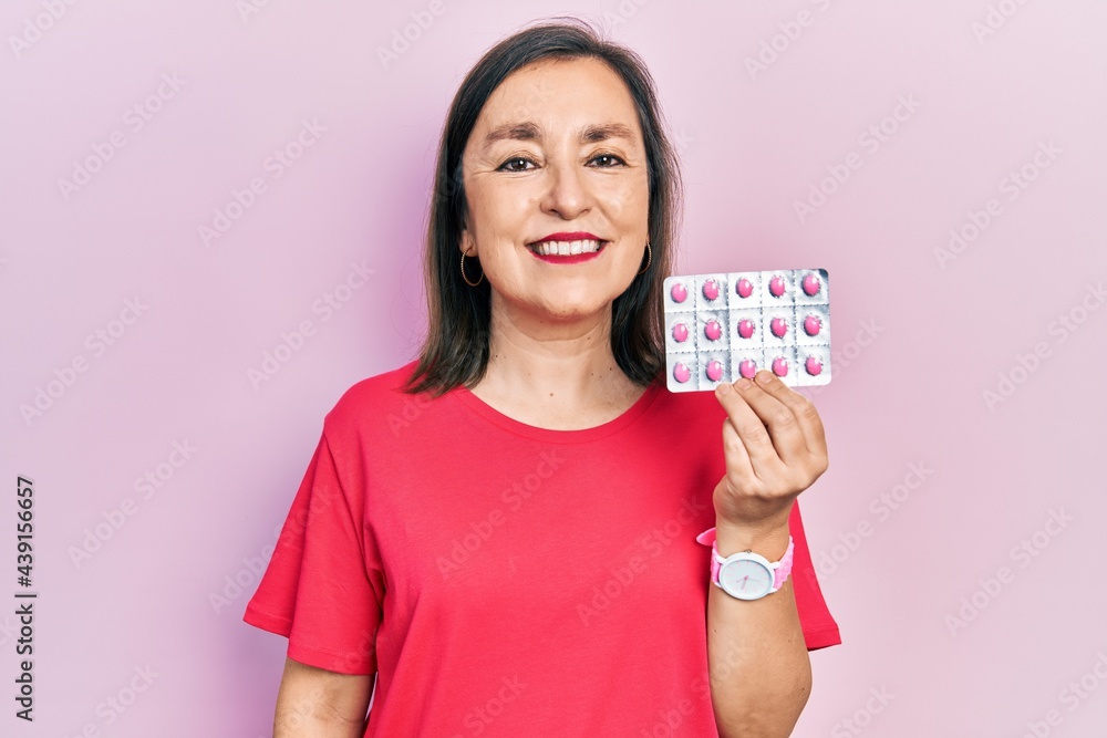 Middle age hispanic woman holding pills looking positive and happy standing and smiling with a confident smile showing teeth Middle age hispanic woman holding pills looking positive and happy standing and smiling with a confident smile showing teeth