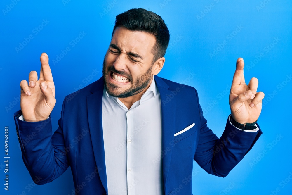 Young hispanic businessman wearing business jacket gesturing finger crossed smiling with hope and eyes closed. luck and superstitious concept. Young hispanic businessman wearing business jacket gesturing finger crossed smiling with hope and eyes closed. luck and superstitious concept.