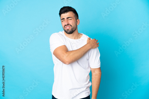 Caucasian man over isolated blue background suffering from pain in shoulder for having made an effort