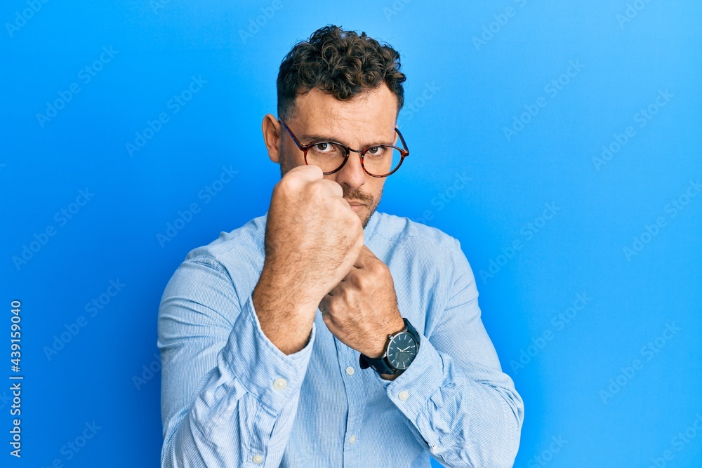 Young hispanic man wearing casual clothes and glasses ready to fight with fist defense gesture, angry and upset face, afraid of problem Young hispanic man wearing casual clothes and glasses ready to fight with fist defense gesture, angry and upset face, afraid of problem