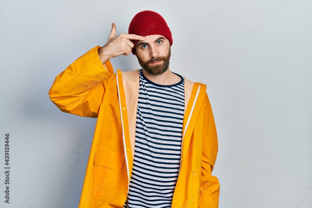 Caucasian man with beard wearing yellow raincoat pointing unhappy to pimple on forehead, ugly infection of blackhead. acne and skin problem Caucasian man with beard wearing yellow raincoat pointing unhappy to pimple on forehead, ugly infection of blackhead. acne and skin problem