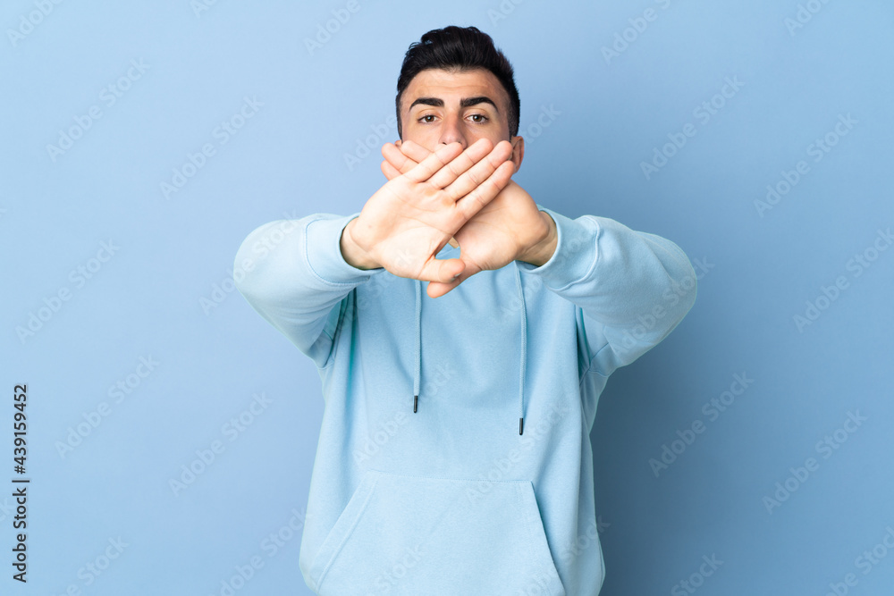 Caucasian man over isolated blue background making stop gesture with her hand to stop an act