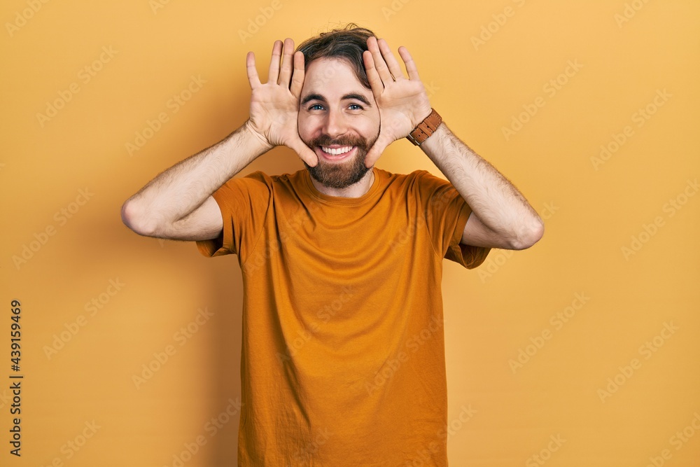 Caucasian man with beard wearing casual yellow t shirt smiling cheerful playing peek a boo with hands showing face. surprised and exited Caucasian man with beard wearing casual yellow t shirt smiling cheerful playing peek a boo with hands showing face. surprised and exited
