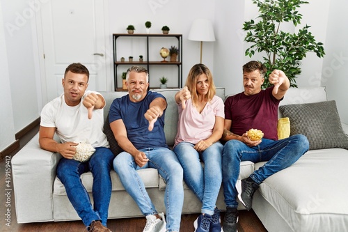 Group of middle age people sitting on the sofa at home looking unhappy and angry showing rejection and negative with thumbs down gesture. bad expression.