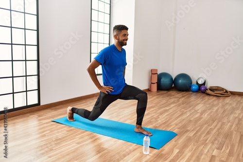 Handsome hispanic man doing exercise and stretching on yoga mat, practicing flexibility and training at the gym