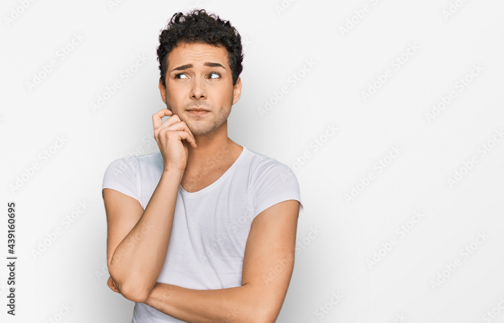 Young handsome man wearing casual white t shirt serious face thinking about question with hand on chin, thoughtful about confusing idea Young handsome man wearing casual white t shirt serious face thinking about question with hand on chin, thoughtful about confusing idea