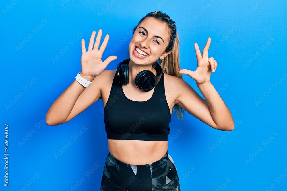 Beautiful hispanic woman wearing gym clothes and using headphones showing and pointing up with fingers number eight while smiling confident and happy. Beautiful hispanic woman wearing gym clothes and using headphones showing and pointing up with fingers number eight while smiling confident and happy.
