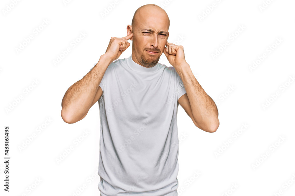 Fototapeta premium Bald man with beard wearing casual white t shirt covering ears with fingers with annoyed expression for the noise of loud music. deaf concept.