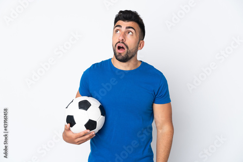 Handsome young football player man over isolated wall looking up and with surprised expression