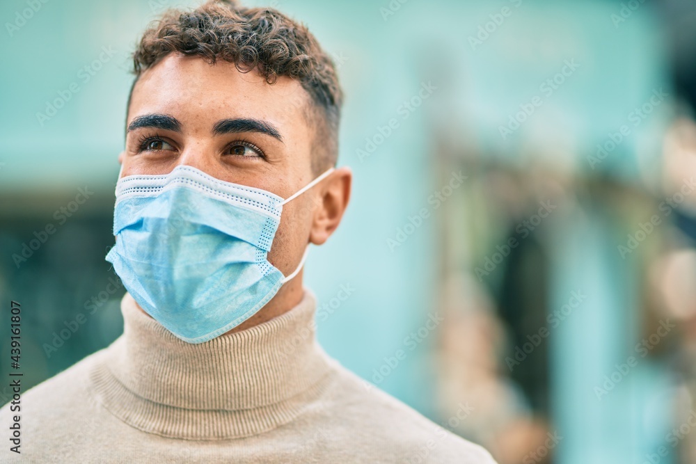 Young hispanic man wearing medical mask standing at the city.