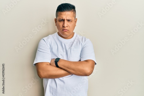 Young latin man wearing casual white t shirt skeptic and nervous, disapproving expression on face with crossed arms. negative person.