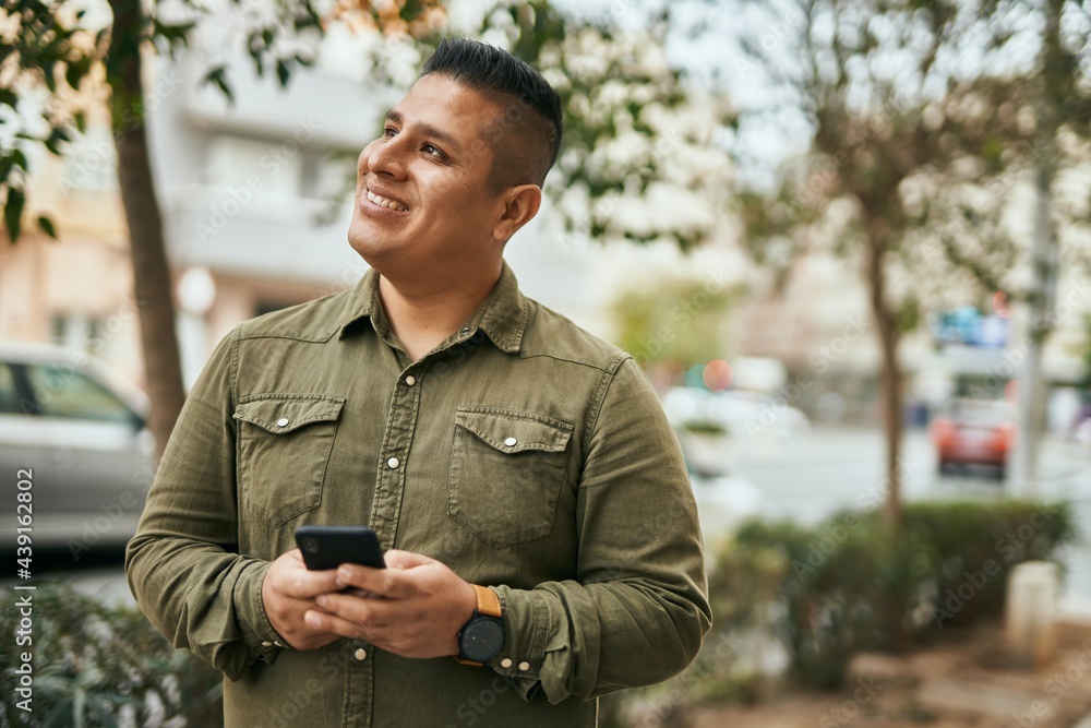Young latin man smiling happy using smartphone at the city. Young latin man smiling happy using smartphone at the city.